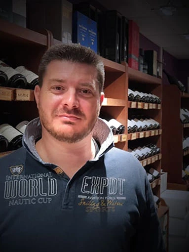 Guillaume Nicolas, caviste expert chez As du Vin à Dijon, posant devant les rayonnages de bouteilles de vin de la boutique.