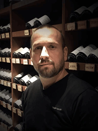 Castells François-Xavier, caviste expert chez As du Vin à Dijon, posant devant les rayonnages de bouteilles de vin de la boutique.